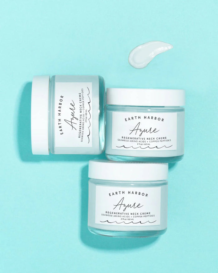 Three jars of Earth Harbor AZURE Smooth Neck + Face Water Cream rest on a light blue background. One jar is open, displaying a bit of cream nearby. The label features nourishing seaweed and rejuvenating copper peptides as the main ingredients for radiant skin.