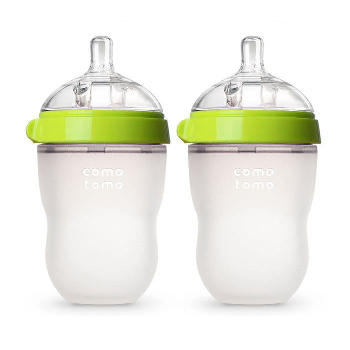 Two Comotomo Baby Bottles with green lids and silicone nipples are displayed upright. These anti-colic bottles have a wide neck and squeezable body, ideal for smooth breastfeeding transitions.