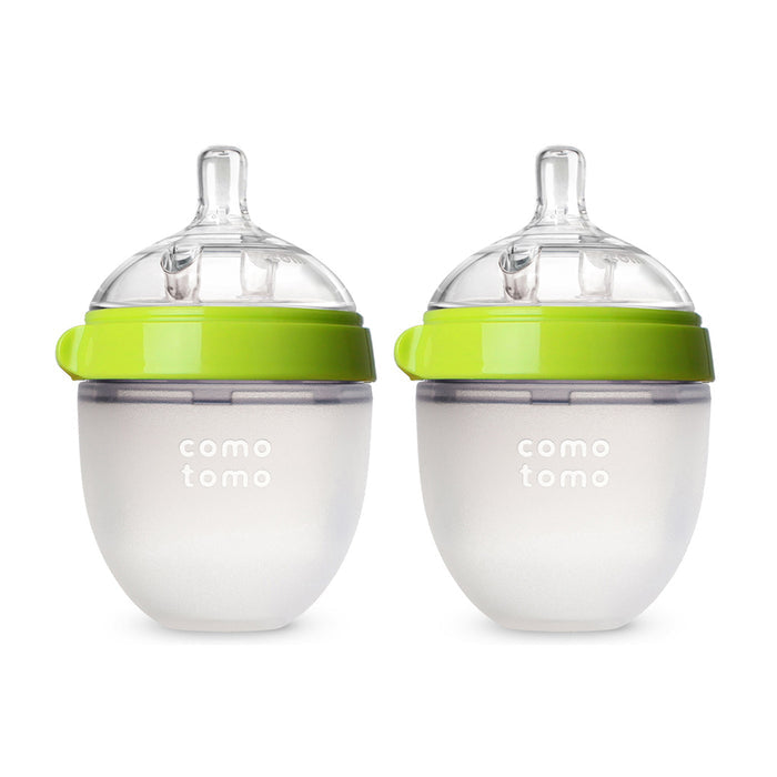 The Comotomo Baby Bottle Gift Set includes two translucent bottles with green lids and clear silicone nipples, featuring anti-colic design and a rounded shape that mimics breastfeeding. They are displayed side by side on a white background.
