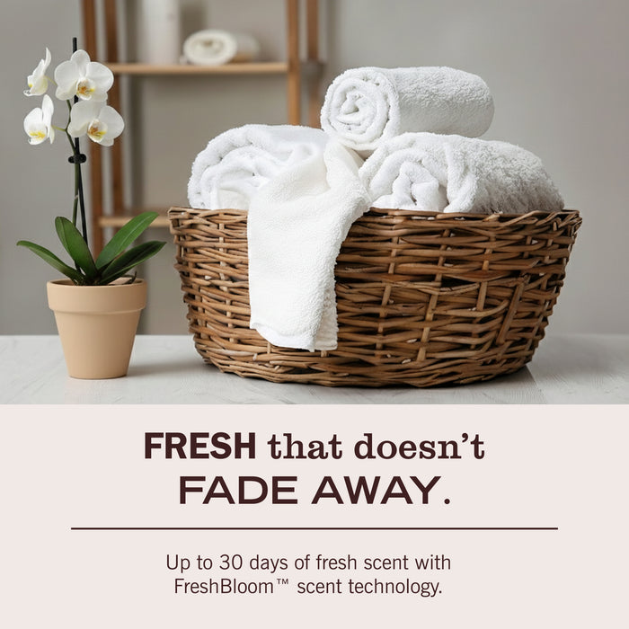 A wicker basket with neatly rolled white towels sits on a table beside a potted white orchid. Text reads: FRESH that ENDURES. Experience up to 30 days of gentle scent with Mrs. Meyer’s FreshBloom™ Baby Laundry Detergent, crafted with naturally derived ingredients. Specially made for your nursery, this detergent keeps baby clothes clean and delicately fresh wash after wash.
