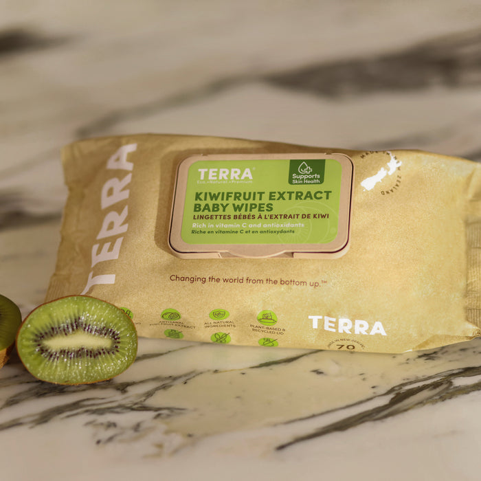 The package of Terra Baby Wipes - Kiwi Fruit on a marble surface showcases green labeling and a sliced kiwi. The text emphasizes natural moisturizing benefits with kiwi ingredients and vitamin C.