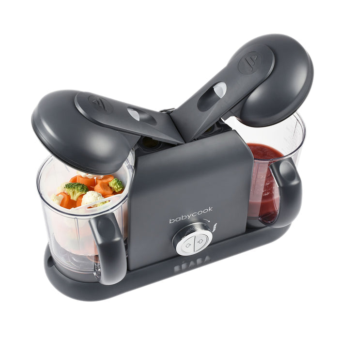 The BEABA Babycook Duo Baby Food Maker, featuring a sleek gray design, is perfect for homemade baby food. One container holds chopped veggies like carrots and broccoli, while the other contains a red puree. It offers one-handed operation for ultimate convenience.