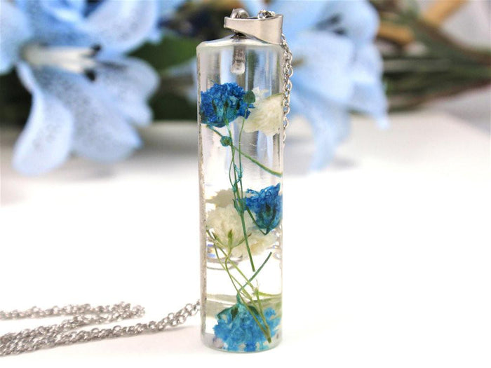 Glass pendant necklace containing blue and white baby's breath preserved in clear resin with infused ashes.