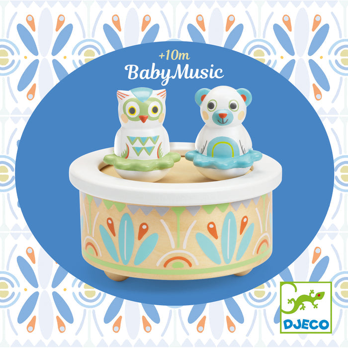 DJecos Babys First Music Box, made from FSC® Certified Wood, is a colorful childrens gift featuring two animal figures—an owl and a bear—with pastel geometric patterns. The box reads +10m BabyMusic alongside the Djeco logo.