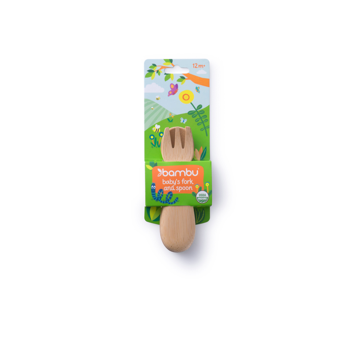A bamboo baby fork and spoon set package labeled bambu in green, highlighting organic bamboo utensils. The packaging showcases vibrant nature illustrations with trees, hills, and the sun. Suitable for ages 12 months and up.