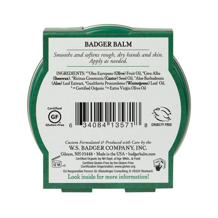 The image shows the back of a green circular tin labeled Badger Balm for Hardworking Hands with details on organic ingredients, barcodes, gluten-free and cruelty-free certifications, and manufacturing info by W.S. Badger Company, Inc.