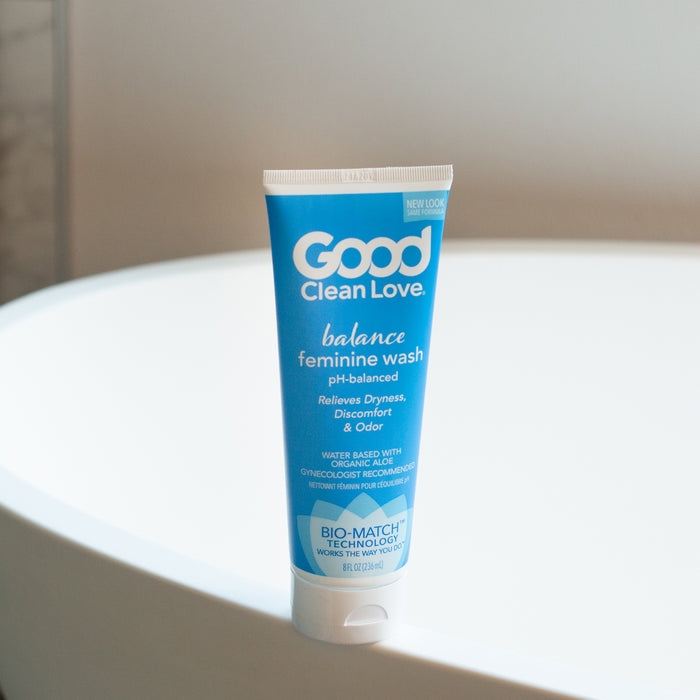 A blue tube of Good Clean Love Balance Moisturizing Wash sits on a white bathroom surface, highlighting its pH-balanced formula that alleviates dryness, discomfort, and odor with Bio-Match™ Technology.