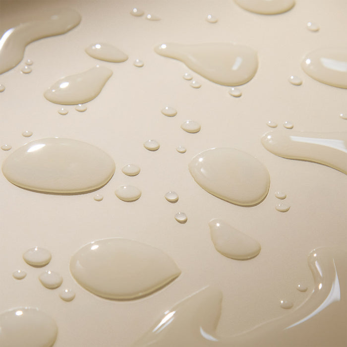 Close-up of clear water droplets on a smooth, beige surface, evoking the fresh, glossy finish of Wildcraft Balance Toner and highlighting its hydrating essence with a radiant, reflective effect.
