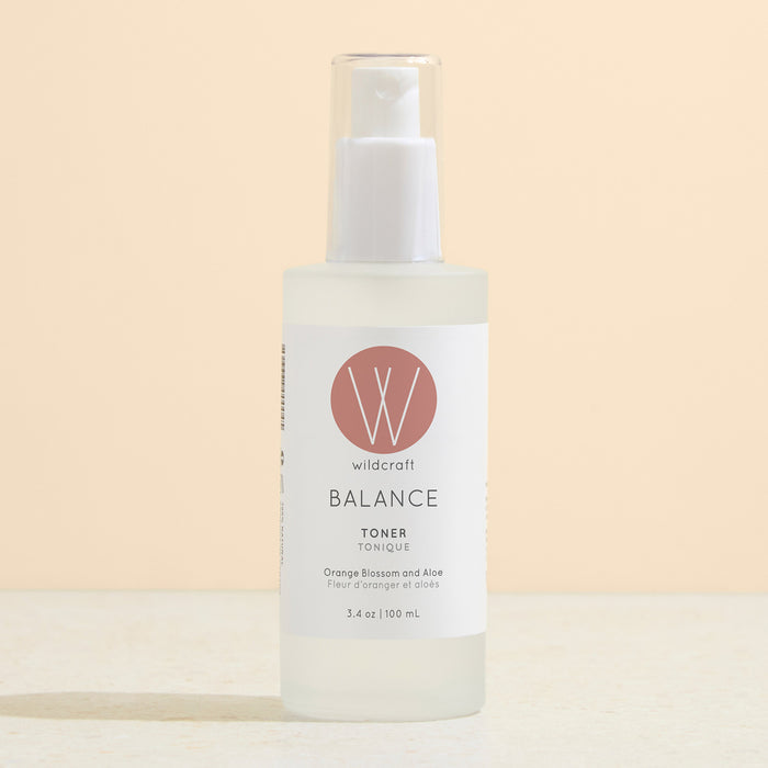 A clear frosted bottle of Wildcraft Balance Toner with a white pump and pink label rests on a light surface against a beige background.