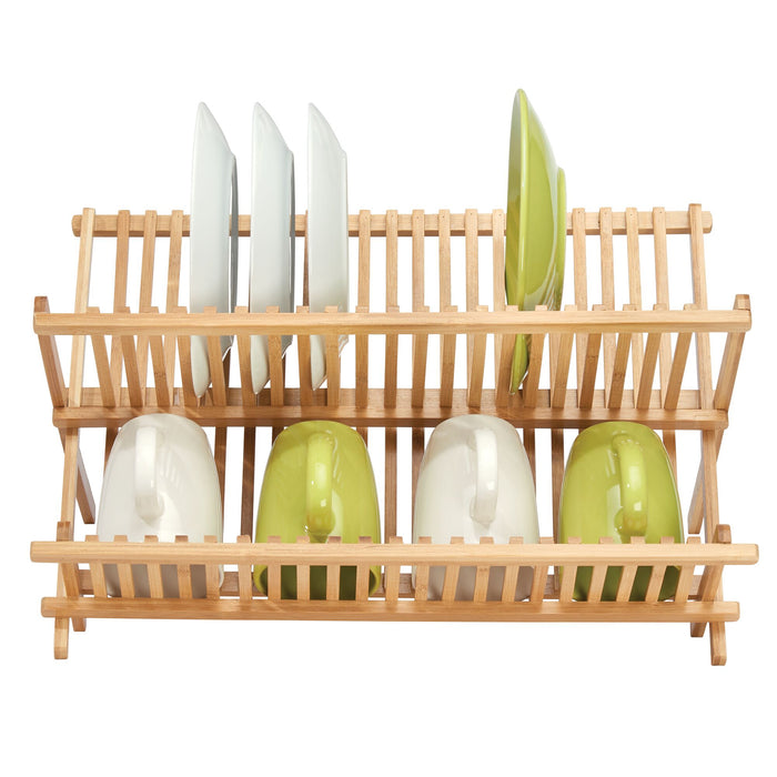 A top view shows the iDesign Bamboo Folding Collapsible Dish Drying Rack holding four white plates upright on the top tier, and three white mugs with one green mug upside down on the bottom tier. Made from renewable bamboo, its collapsible design is both functional and eco-friendly.