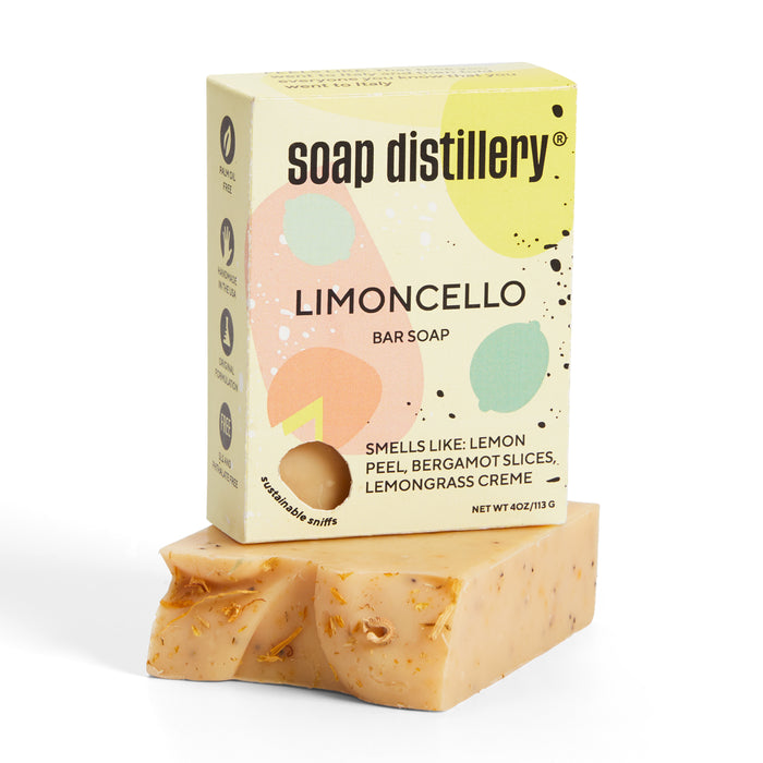 Soap Distillerys Limoncello bar soap, a palm oil-free product, features colorful abstract packaging and an aromatic scent of lemon peel, bergamot slices, and lemongrass creme. The bar has a natural look with visible flecks.
