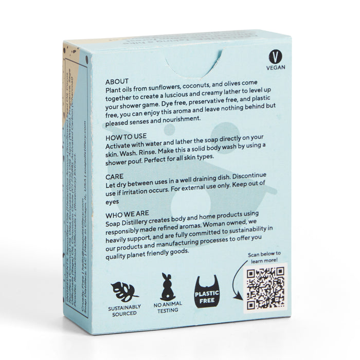 A light blue box features Soap Distillerys vegan bar soap infused with aromatic scents and free from palm oil. It highlights plant oils, usage instructions, and the brands sustainability pledge. Symbols include Vegan, Sustainably Sourced, No Animal Testing, and Plastic Free. A QR code adorns the side.