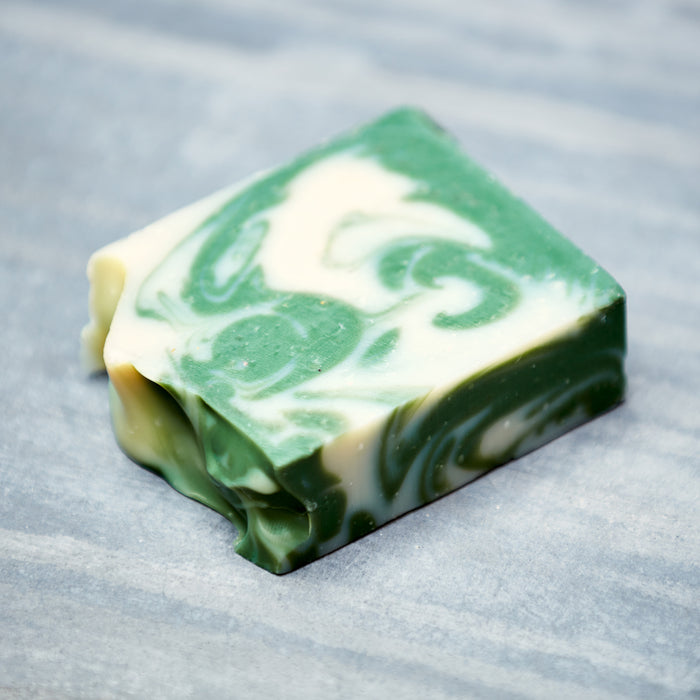 A Bar Soap from Soap Distillery with green and white swirls rests on a gray surface. This artisanal, palm oil-free soap has an irregular shape and smooth edges, offering delightful aromatic scents.
