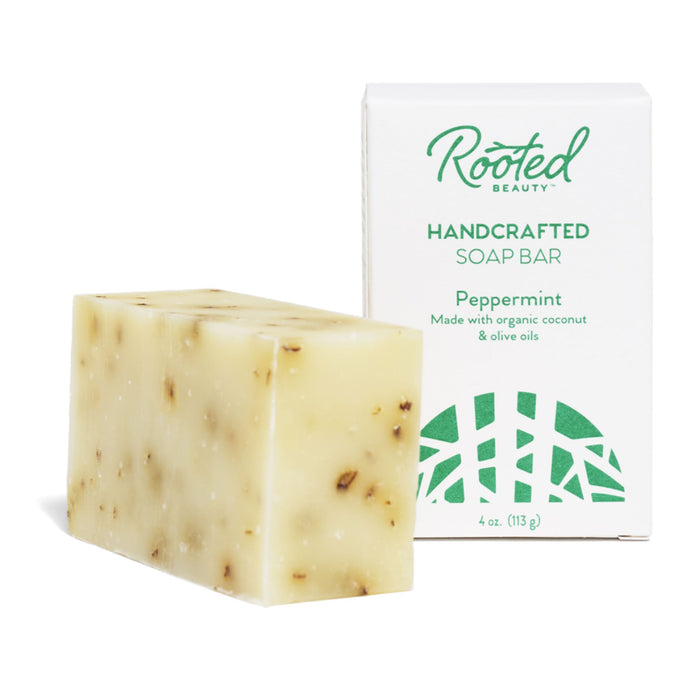 A 4 oz (113 g) cream-colored, cruelty-free Bar Soap with brown flecks sits before its box. The box displays Rooted Beauty Handcrafted Soap Bar, Peppermint, highlighting its blend of organic coconut and olive oils.