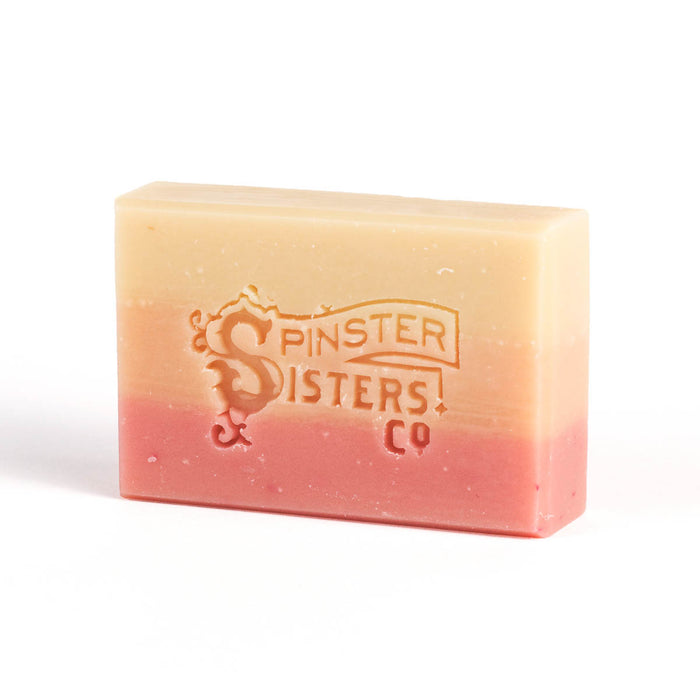 This rectangular vegan bar soap, by Spinster Sisters Co., features a light beige to pink gradient design and an embossed logo with SPINSTER SISTERS CO and a decorative S. It is a moisturizing delight that enhances your bathing routine.