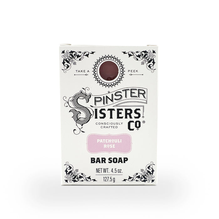 A 4.5 oz Spinster Sisters Co. vegan bar soap in Patchouli Rose scent comes in a white box adorned with black floral designs and a circular cutout showcasing the moisturizing soap inside, labeled Consciously Crafted.