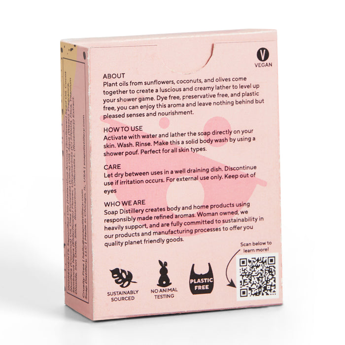 The image shows the back of a pink Soap Distillery Bar Soap box, emphasizing its plant-based ingredients and aromatic scents. It includes usage tips, highlights icons for being palm oil-free, sustainably sourced, cruelty-free, plastic-free, and features a QR code at the bottom.