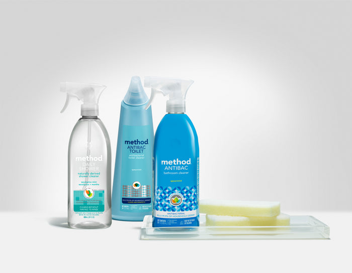 Showcased are three method bathroom cleaning products: a daily shower cleaner in a clear bottle, an antibacterial toilet cleaner in blue, and a bathroom cleaner spray. Nearby, theres a yellow sponge on a clear dish, ideal for use with the method Bathroom Cleaner essentials.