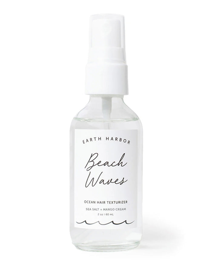 A clear spray bottle labeled BEACH WAVES Ocean Hair Texturizer by Earth Harbor rests against a plain background, containing vegan mango sea salt spray for the perfect beach style. It features a white nozzle and has a capacity of 2 oz / 60 mL.