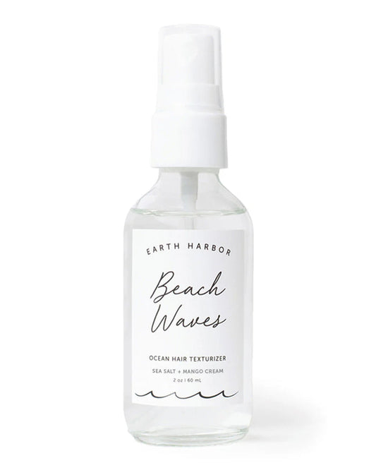 A clear spray bottle labeled BEACH WAVES Ocean Hair Texturizer by Earth Harbor rests against a plain background, containing vegan mango sea salt spray for the perfect beach style. It features a white nozzle and has a capacity of 2 oz / 60 mL.