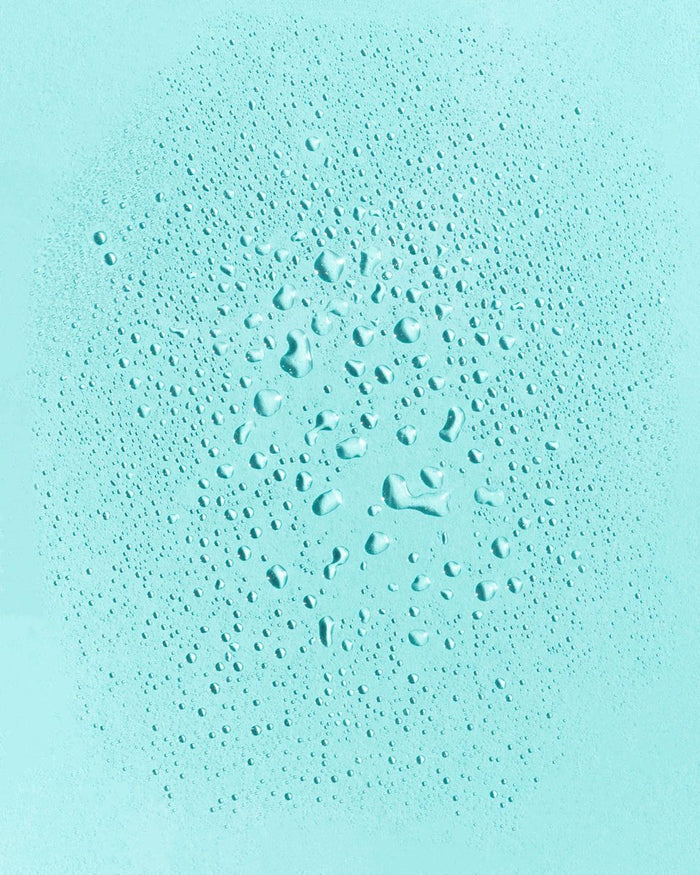 Water droplets on a light blue surface reflect the refreshing vibe of BEACH WAVES Ocean Hair Texturizer by Earth Harbor. The varied sizes form a central cluster, reminiscent of its mango sea salt essence that provides a perfect summery beach style touch.