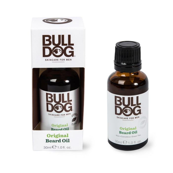 A 30ml Bulldog Beard Oil bottle stands beside its open packaging designed for mens skincare, featuring aloe vera and green tea. The minimalist label displays bold text and a dog logo, emphasizing the richness of essential oils inside.