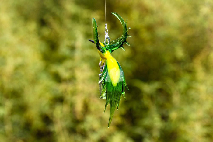 Handmade glass bee eater bird in green and yellow with a sterling silver keepsake urn pendant hanging from its body.