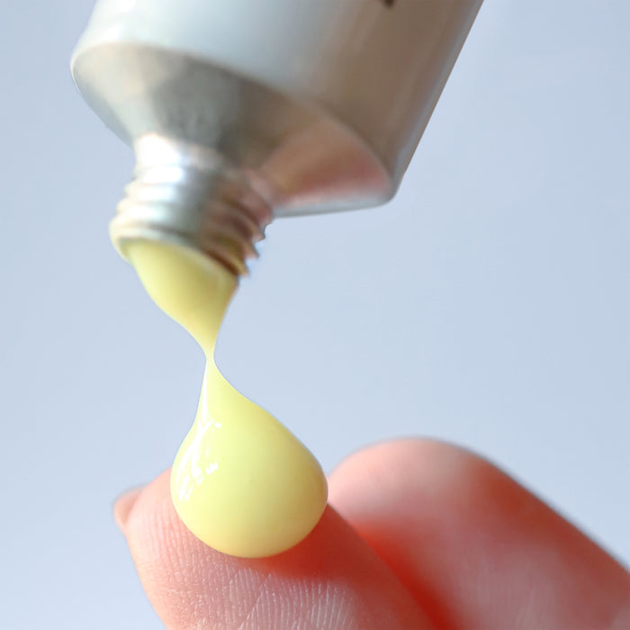 A close-up shows a fingertip with Cocokinds Beginner Retinol Gel, displaying the National Eczema Association Seal of Acceptance™, as its dispensed from a tube. The bright yellow gel glistens against the soft blue background.