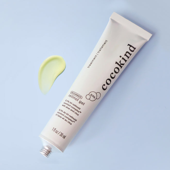 On a light blue surface, a white tube of Cocokinds Beginner Retinol Gel appears with a small dab of its light yellow gel next to it. The tube displays product details and features the National Eczema Association Seal of Acceptance™.