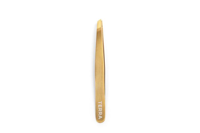 Slanted gold tweezers, engraved with TERRA at the base, elegantly displayed on a white background as part of the Beheld Brow Kit by Terra Beauty Bars.