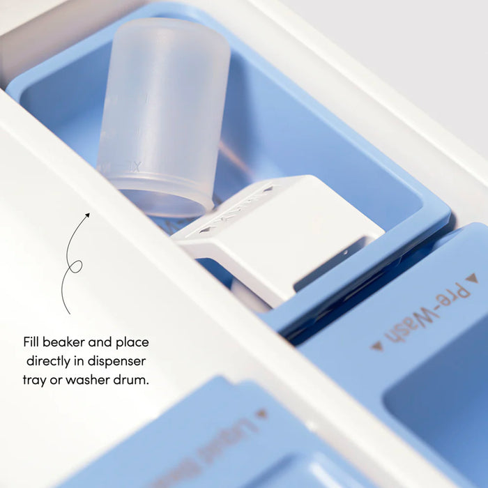 A close-up of a washing machine detergent dispenser featuring a beaker and clearly labeled compartments. Text instructs to fill the beaker with Dirty Labs Bio Laundry Detergent with Phytolase® - Free & Clear, then place it in the dispenser tray or directly into the washer drum.