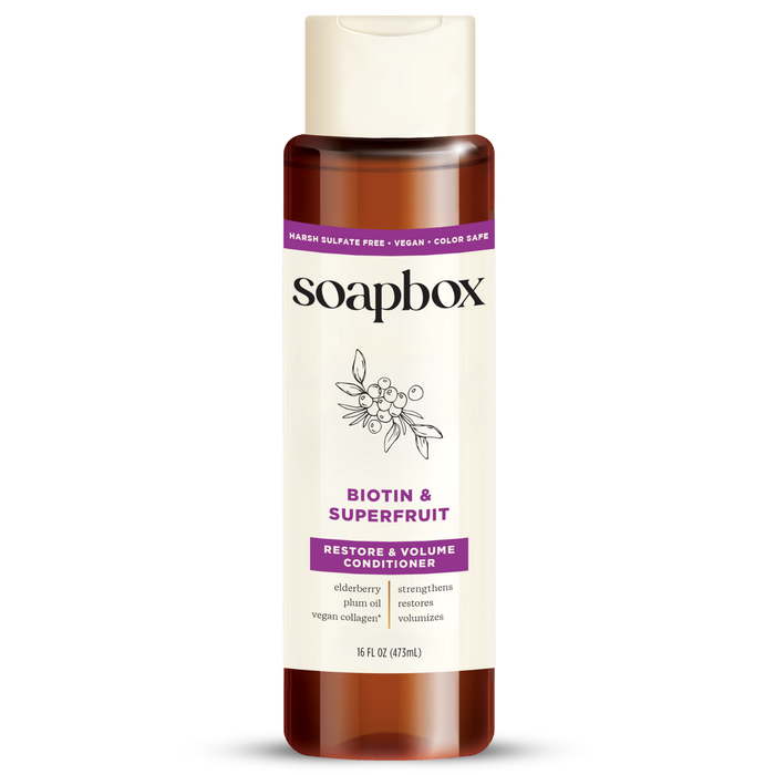 Soapboxs Biotin and Superfruit Restore & Volumize Conditioner is a volumizing, sulfate-free, color-safe conditioner infused with vegan collagen. It features a berry illustration and comes in a 16 fl oz (473 ml) bottle with a brown top and white body.