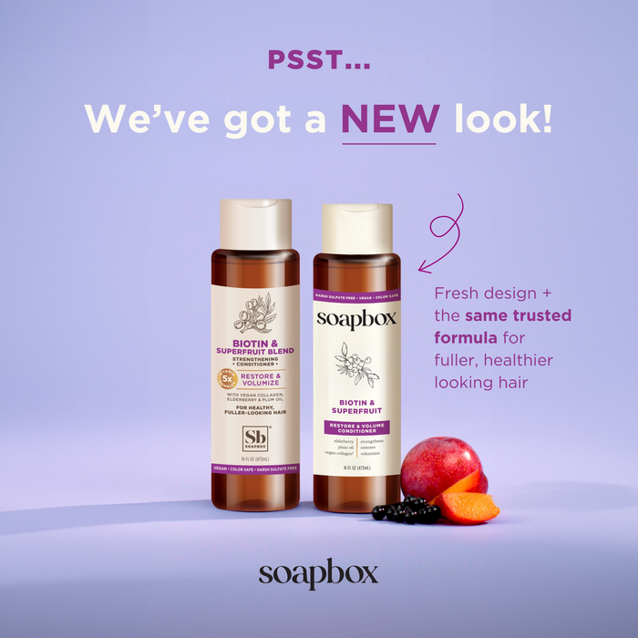 Two Soapbox Biotin and Superfruit Restore & Volumize Conditioner bottles against a purple background with berries. The fresh design features vegan collagen and biotin for fuller, healthier hair. Heading: Weve got a NEW look!.