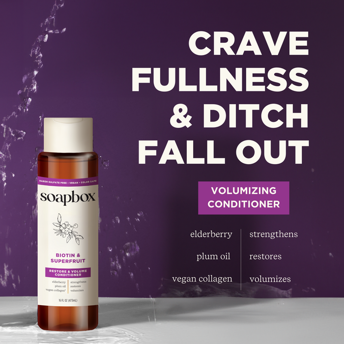 A Soapbox Biotin and Superfruit Restore & Volumize Conditioner bottle sits on a wet surface. The background reads Crave Fullness & Ditch Fall Out, emphasizing biotin, elderberry, plum oil, vegan collagen, and its volumizing benefits.
