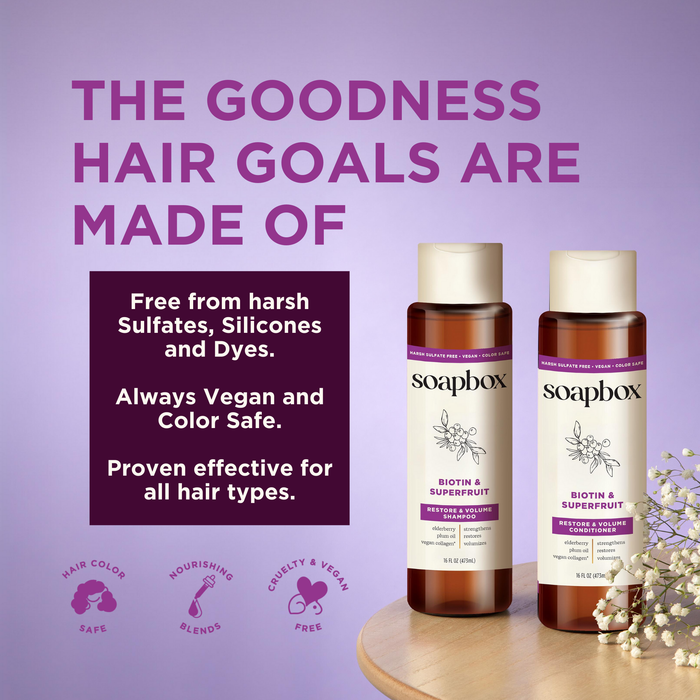 Two bottles of Soapbox Biotin and Superfruit Restore & Volumize Shampoo sit on a wooden surface. The lavender text highlights their benefits: free from sulfates, silicones, and dyes; infused with vegan collagen; color-safe; cruelty-free; suitable for all hair types.