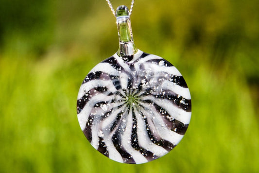 Black and white circular glass pendant with a starburst swirl and ash specks on a silver chain.