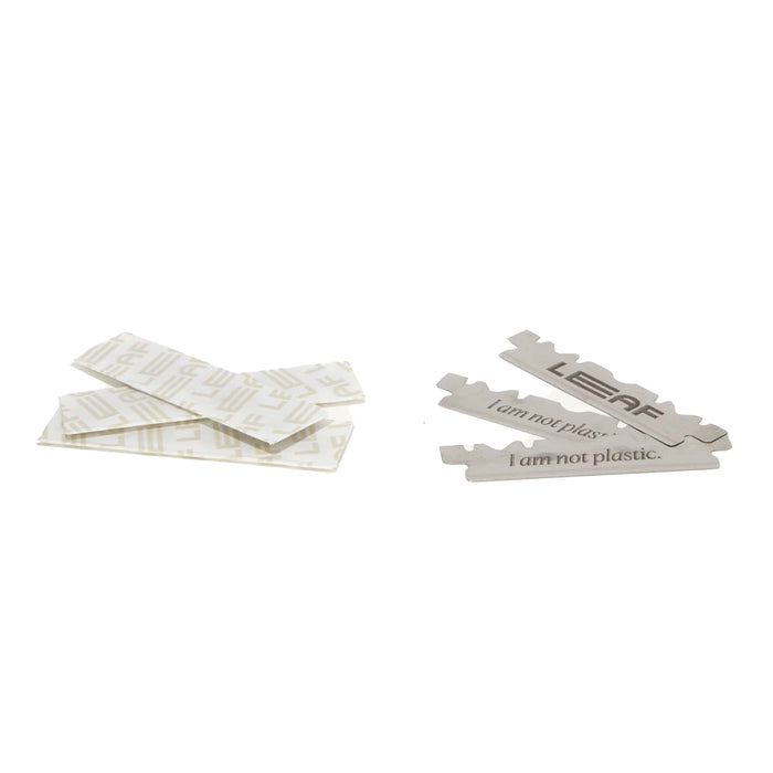 Four metallic Leaf etched blades, featuring I am not plastic, and several wrapped ones are displayed on a white background. These stainless steel blades from the Leaf Shave Blade Refills reflect a pledge to sustainable shaving.