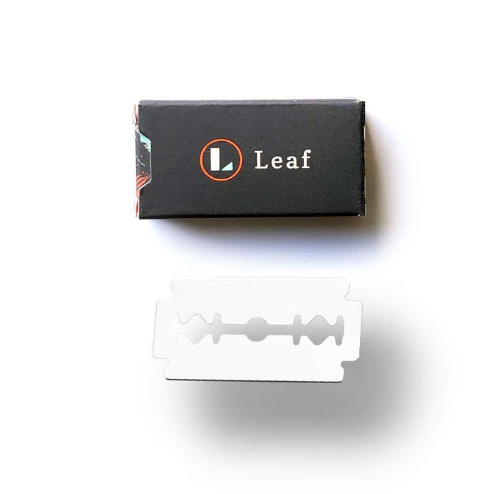 A double-edged stainless steel razor blade is shown in front of a sleek black box labeled Leaf with an orange circle logo. The Leaf Shave Blade Refills showcase a minimalist design, emphasizing sustainable shaving on a plain white background.