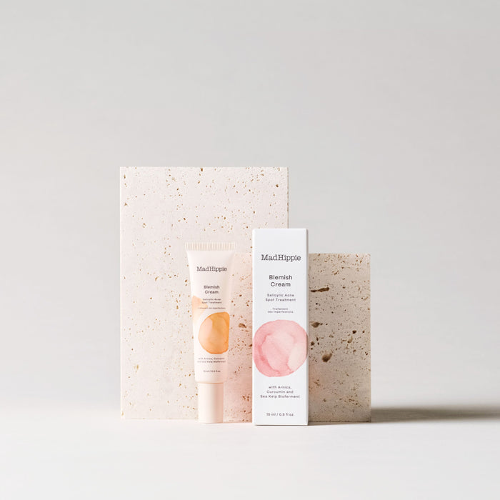 Displayed against a textured beige backdrop, the Mad Hippie Blemish Creams tube and box feature soft pink and peach circular brushstroke designs, hinting at its gentle strength for effective spot treatment.