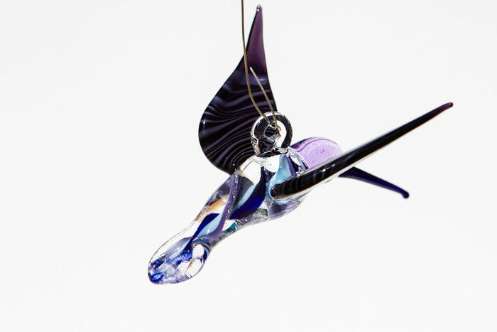 Hanging glass hummingbird with cremation ashes, blue and purple swirls, shown from a side view with a top hook.