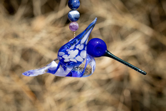 Blue glass hummingbird ornament with crushed opal in the body and a beaded strand of sodalite and amethyst beads.