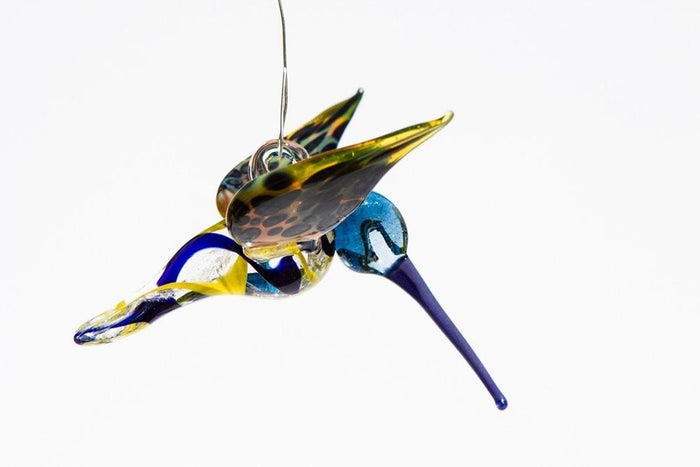 Side view of a blue and yellow glass hummingbird infused with ashes and a hanging hook.
