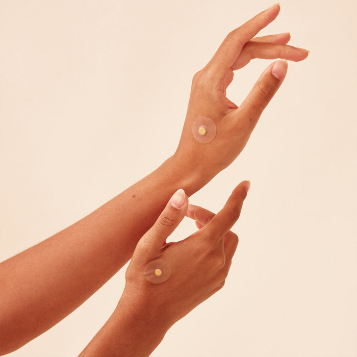 Two hands elegantly posed against a neutral background, each adorned with a small, round Body Balance Magnet from WTHN, subtly suggesting the beginning of a wellness journey. The slightly curled fingers and warm skin tone contribute to the serene ambiance.