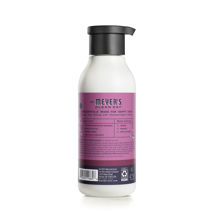 A Mrs. Meyers Body Lotion bottle features a purple label with white text describing its naturally derived ingredients and garden-inspired scents. The image shows the back of the bottle with a sleek black pump dispenser.