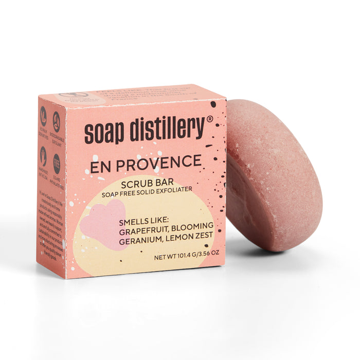 The Body Scrub Bar from Soap Distillery comes in a plastic-free box with pink-toned branding, featuring scents of grapefruit, blooming geranium, and lemon zest. The solid exfoliating bar moisturizes and can stand upright next to its packaging.
