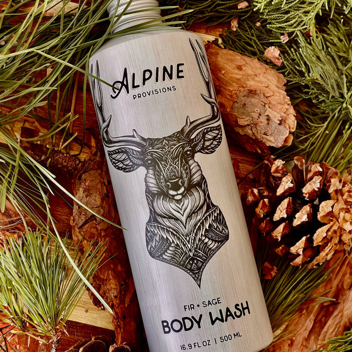 An Alpine Provisions Body Wash with a stylized deer head among pinecones contains natural essential oils. The label notes the volume as 16.9 fl oz (500 mL).