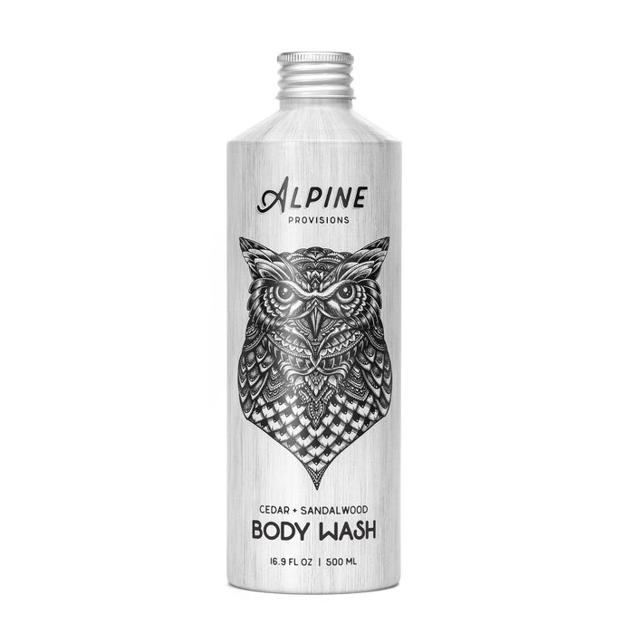 A silver bottle of Alpine Provisions body wash featuring an intricate black owl illustration on the front. The label notes the scents as cedar and sandalwood and the volume as 16.9 fl oz (500 ml).