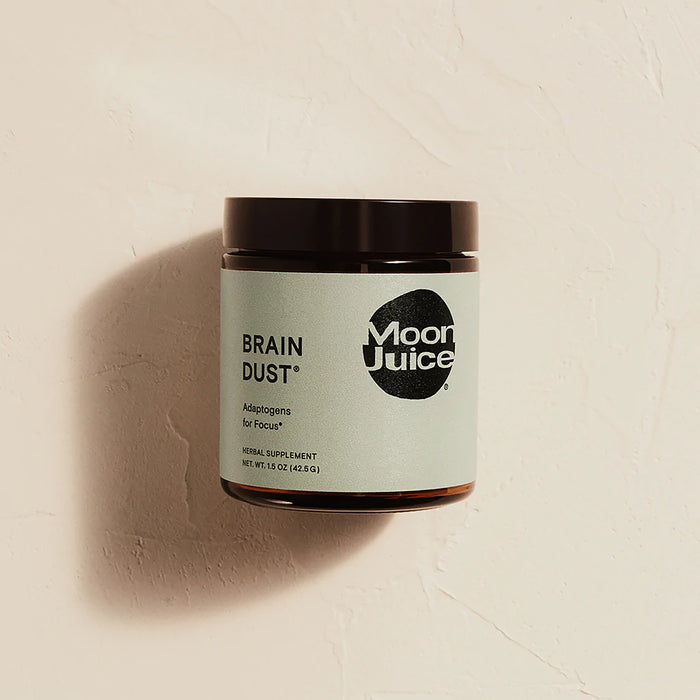 A jar of Moon Juice Brain Dust sits against a textured beige background. The label reads Brain Dust - Adaptogens for Mental Stamina, Alertness & Concentration, emphasizing its nootropic blend. This herbal supplement weighs 1.5 oz (42.5 g).