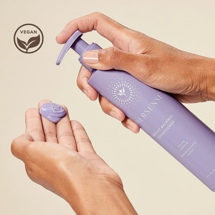 A person is dispensing a purple conditioner onto their hand from a lilac bottle labeled "Hersense Bright Balance Conditioner." A vegan symbol is visible in the corner.