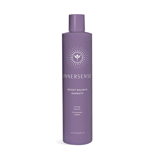 A tall, cylindrical purple bottle labeled Bright Balance Hairbath by Innersense Organic Beauty, featuring a stylized sunburst design. This vegan violet shampoo neutralizes brass tones, set against a plain white background.